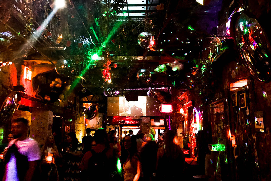 Eine bunte Bar mit Discokugeln, bunten Lichtern und vielen Menschen am Abend.