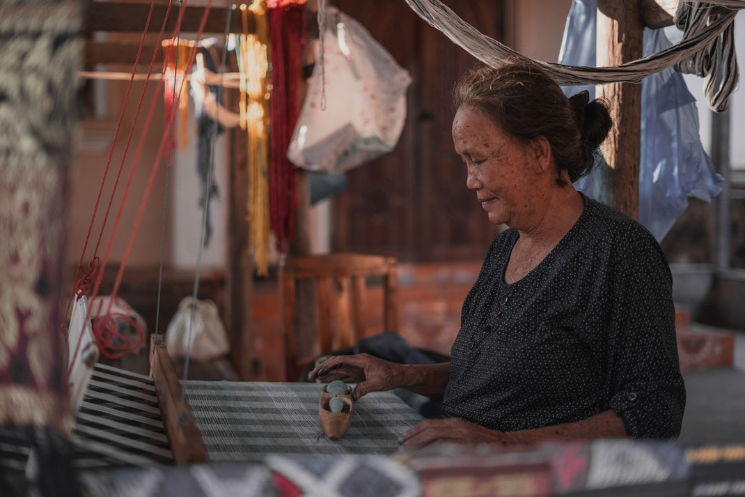 老女が機織り機の前に座り、布を織っている。
