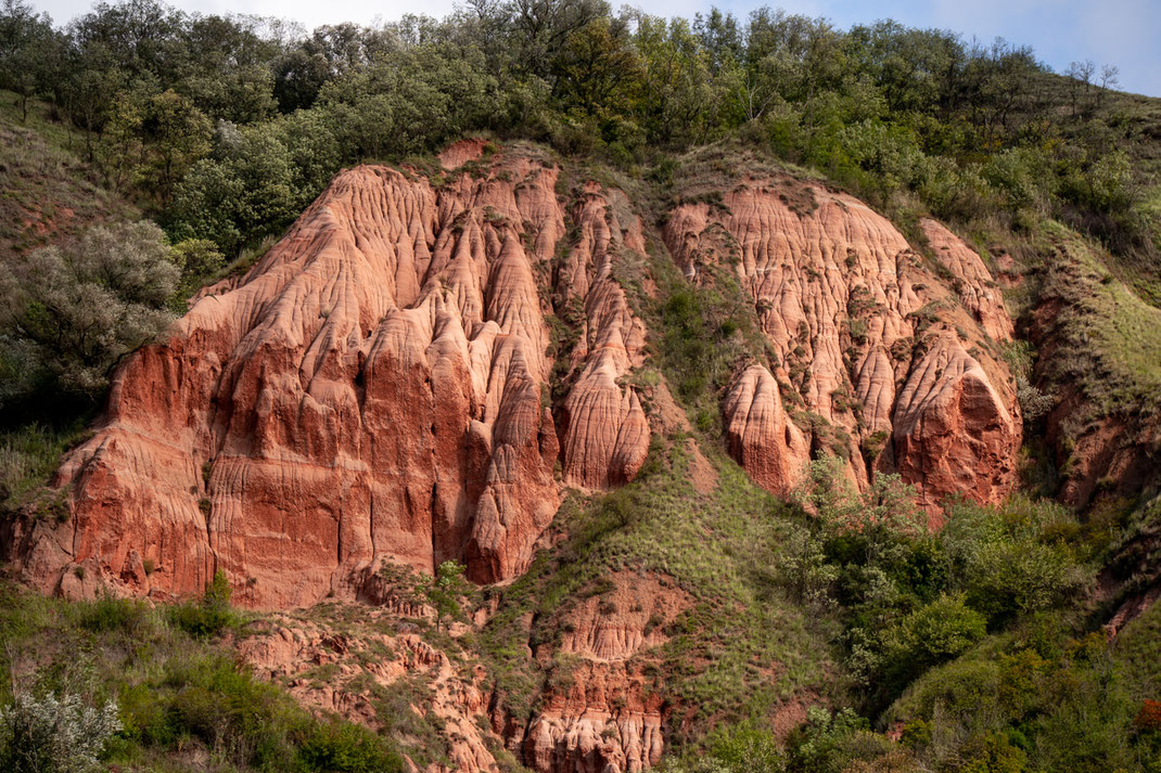 Die skurrile rote Felsformation Râpa Rosie ist von grünen Hügeln eingebettet.