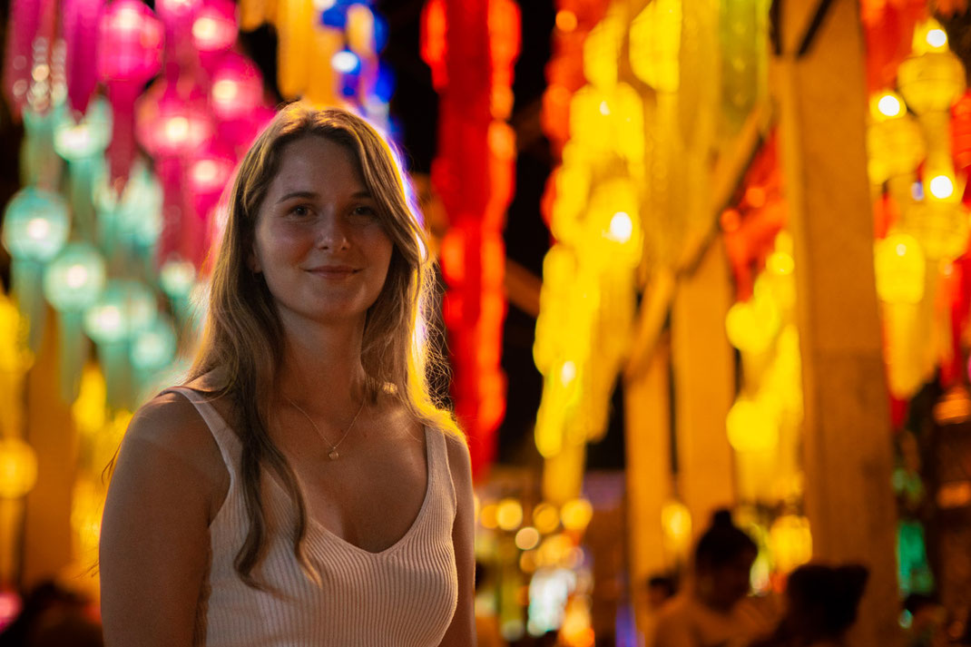 女性がカメラに向かって微笑み、背景には色とりどりのランタンが吊るされている。