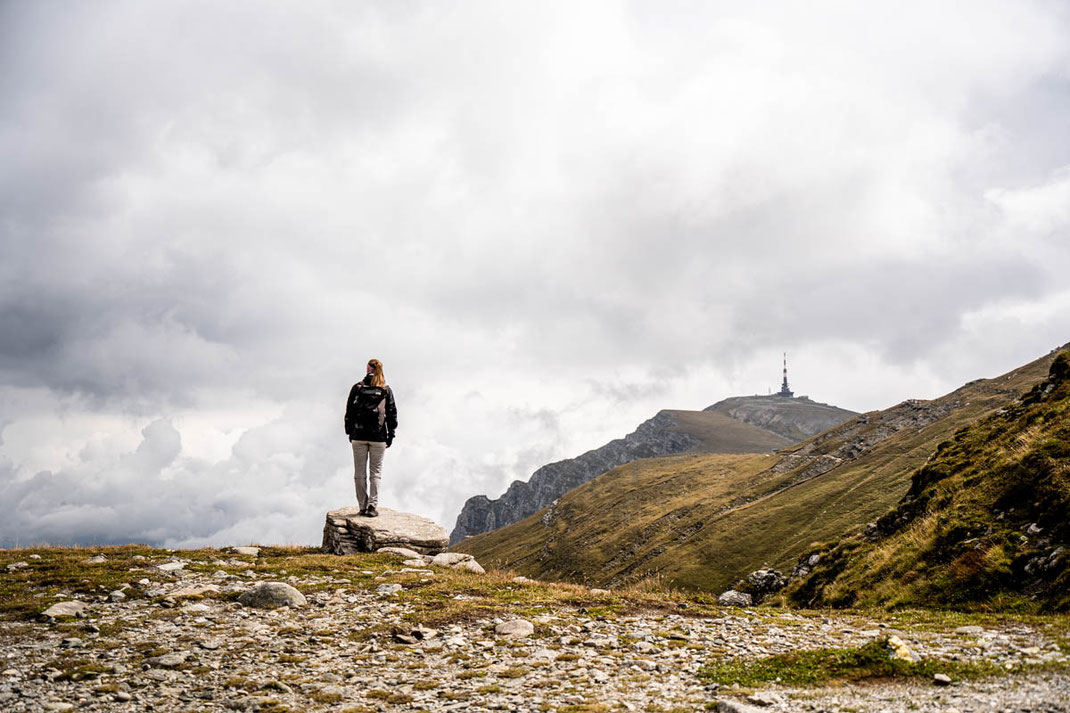 Eine Frau steht auf einen Felsen und blickt auf die Landschaft des Bucegi Nationalparks.