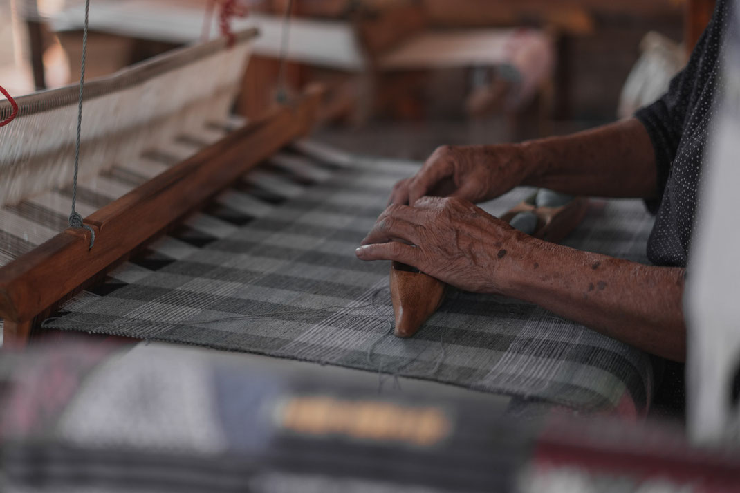 An old woman sits at her loom and works on her fabric.