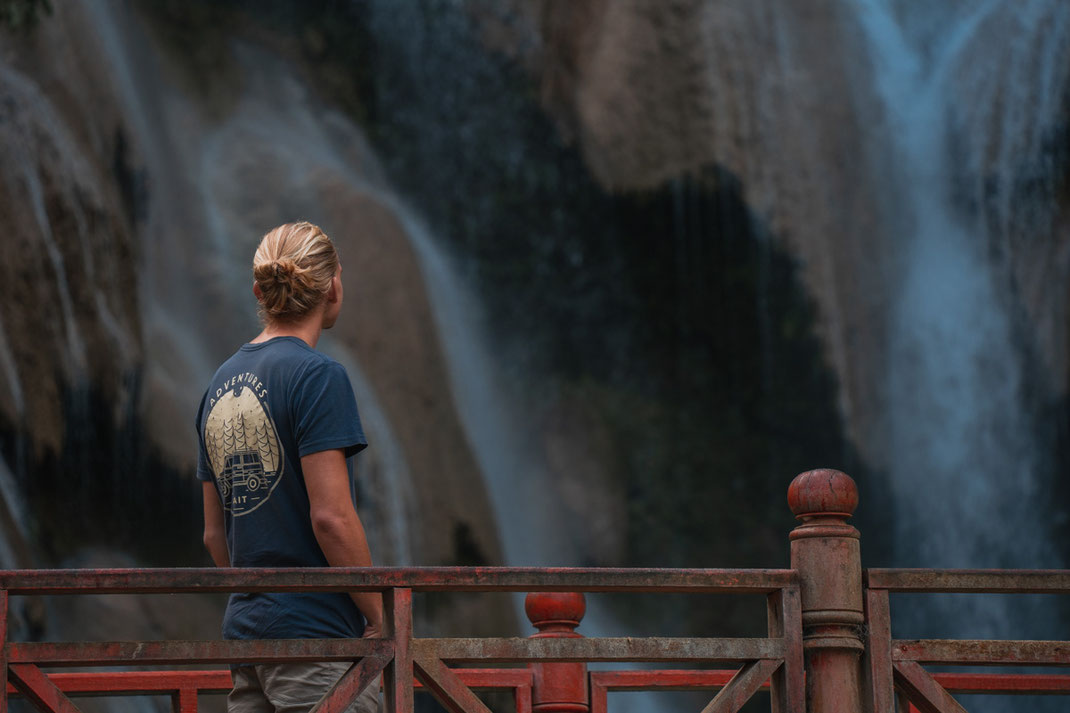 Un homme se tient sur un pont rouge et regarde la chute d'eau Tat Kuang Si.