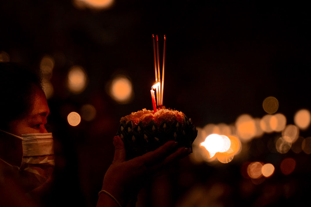 一位妇女将装有蜡烛和香烛的彩色花船放入水中。