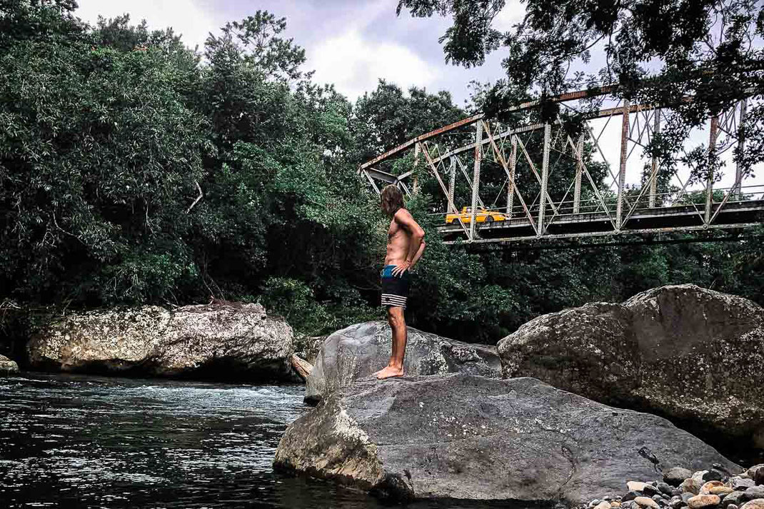 Man standing on the bank of Rio Bermejo and in the background a cab crossing the bridge.