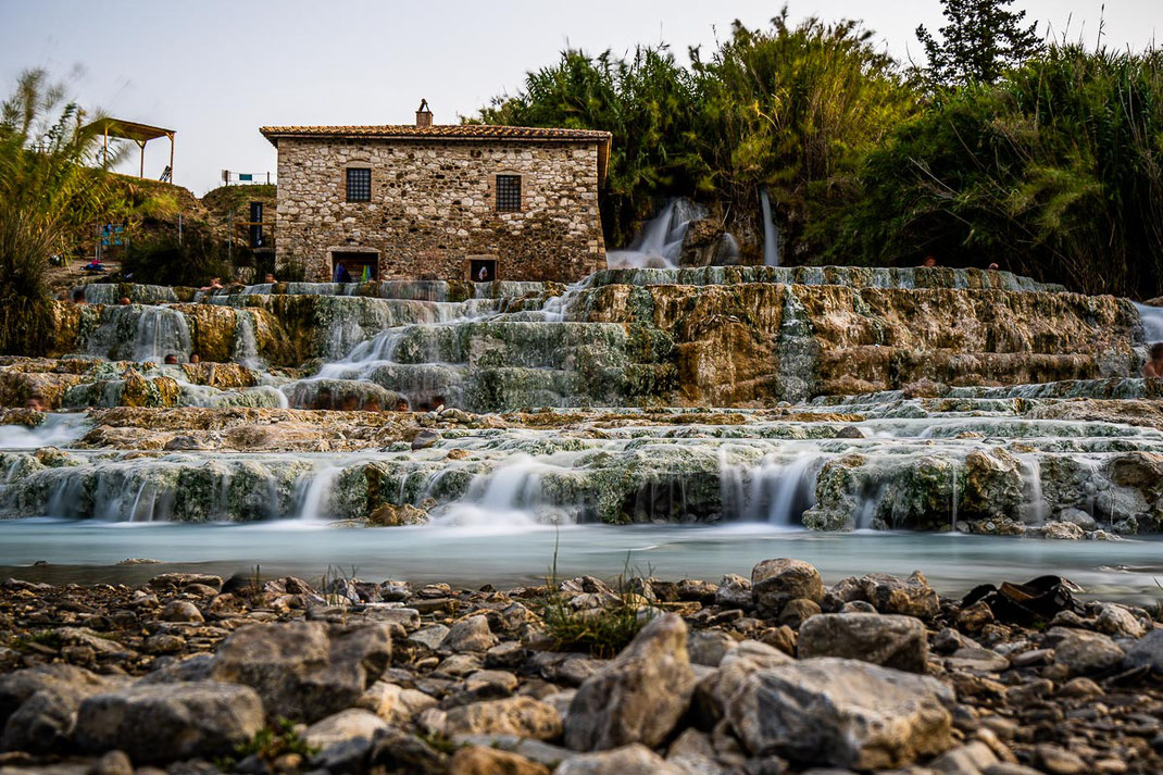 Thermalbad in der Toskana bei Saturnia mit hellblauem Wasser und Haus.