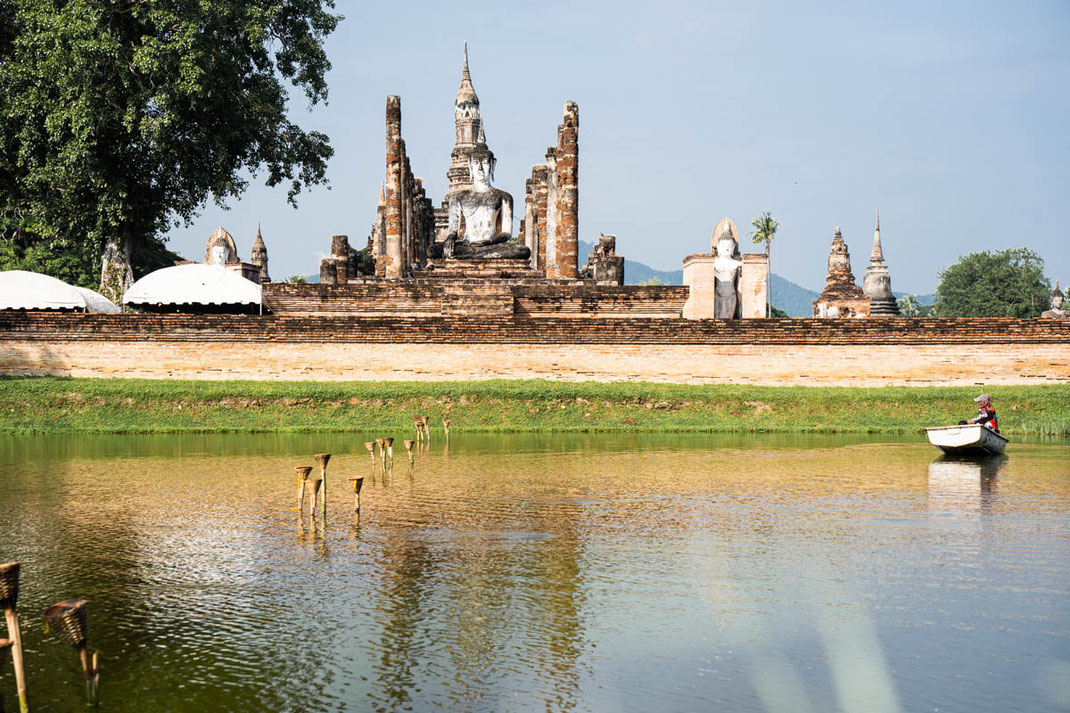 Un antiguo templo con un Buda sentado se encuentra junto a un lago en Sukhothai.