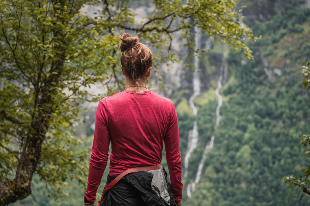 Eine Frau genießt bei einer Wanderung die Aussicht auf einen entfernten Wasserfall am Geiranger Fjord.
