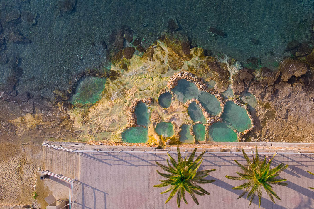 Luftaufnahme von den Heißen Quellen und Becken bei Loutra Edipsos mit Palmen und Meer.