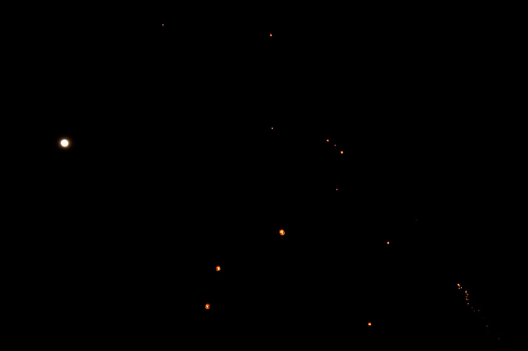 Small bright dots rise up into the night sky of Chiang Mai.