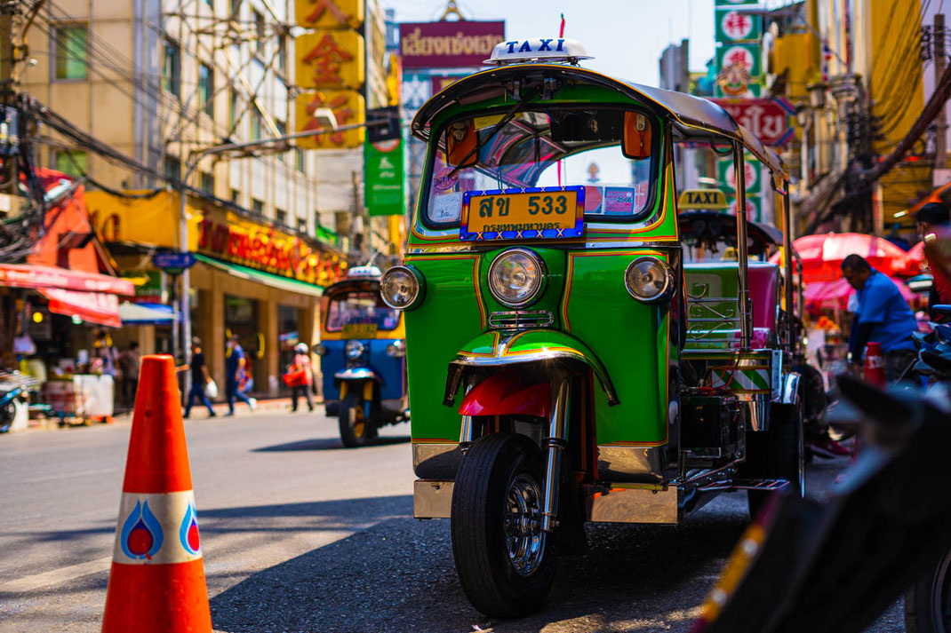 A green, highly polished tuktuk stands on the side of the road in Chinatown.