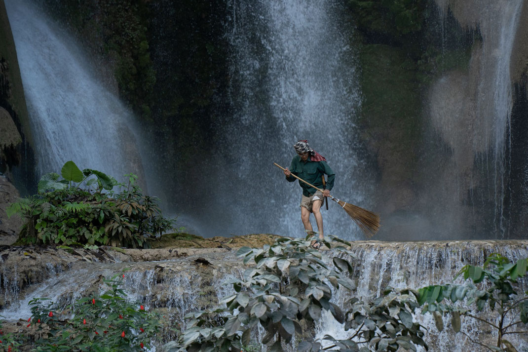 Un homme au pied de la cascade Tat Kuang Si avec un balai.