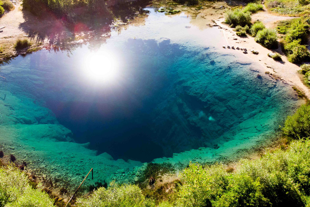 Die Sonne reflektiert sich im spiegelglatten Wasser der Cetina Quelle, von der der Abgrund zu sehen ist. 