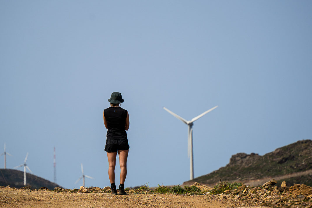 Ein Frau blickt in kurzer Hose und Hut auf die Windräder der Insel Euböa.