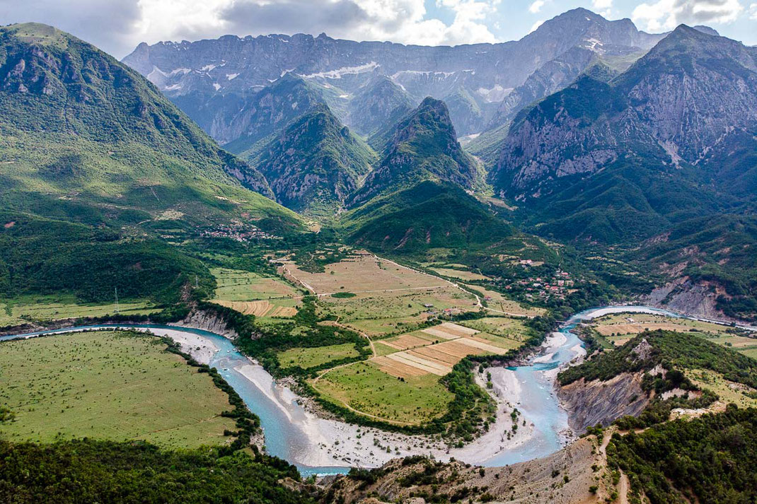 Atemberaubendes Panorama des türkisen Wildflusses Vjosa mit majestätischer Bergkette im Hintergrund.