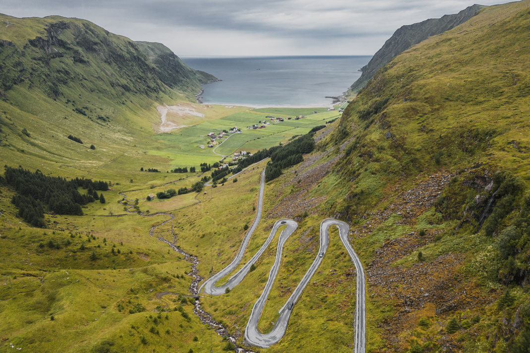 Die Serpentinen führen durch eine grüne, bergige Landschaft hinab nach Hoddevik, einem bekannten Surfstrand in Norwegen.
