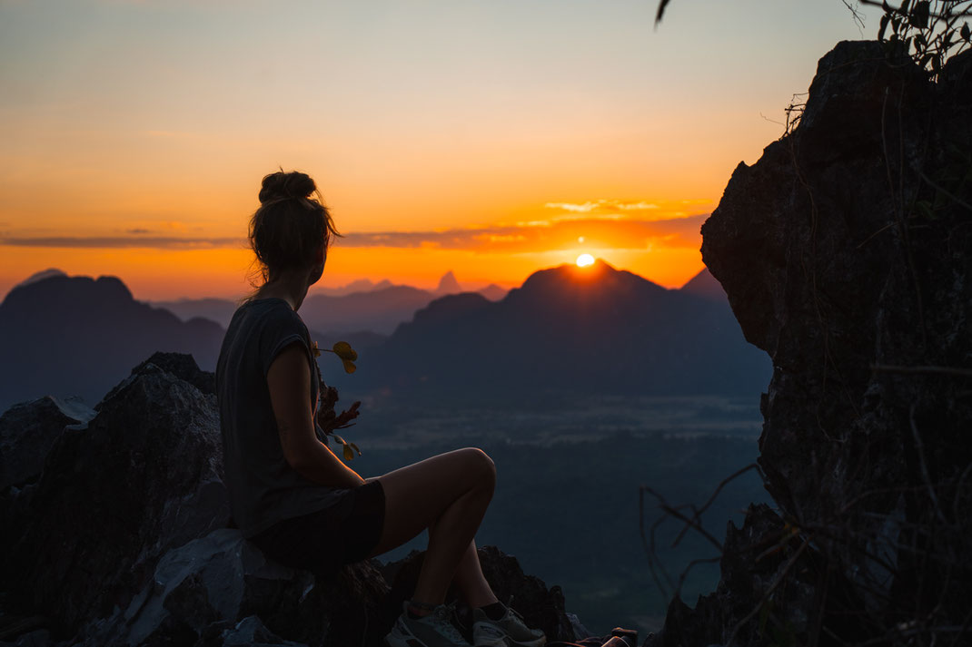 バンビエン近郊で、岩に腰掛けて夕日を眺める女性。
