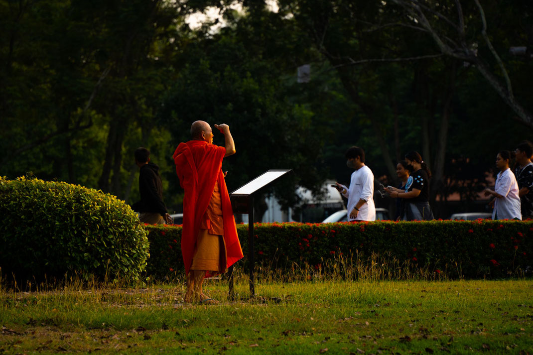 一位僧侣站在草地上，用手遮住眼睛。