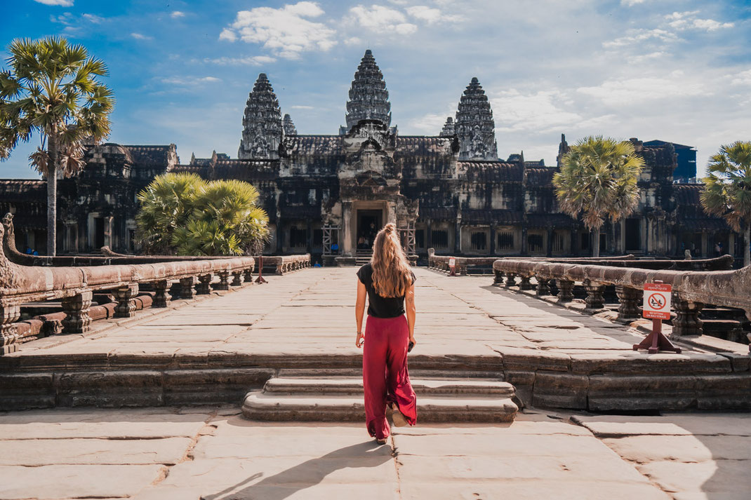 Une femme vêtue d'un pantalon rouge se promène en direction du célèbre Angkor Wat.
