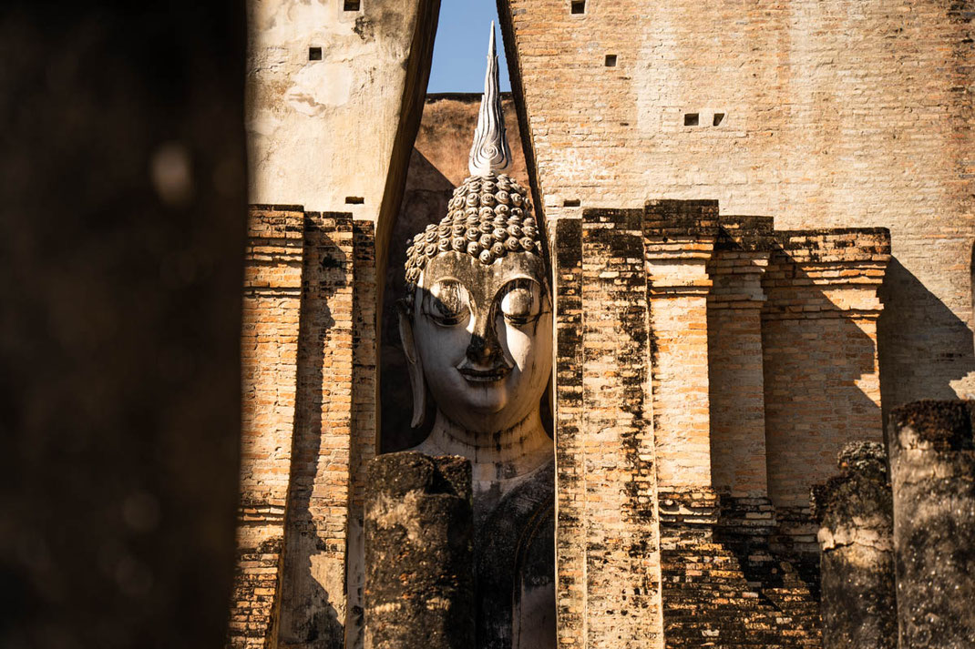 Une énorme figure de Bouddha se glisse dans une mince fente de son bâtiment à Sukhothai.