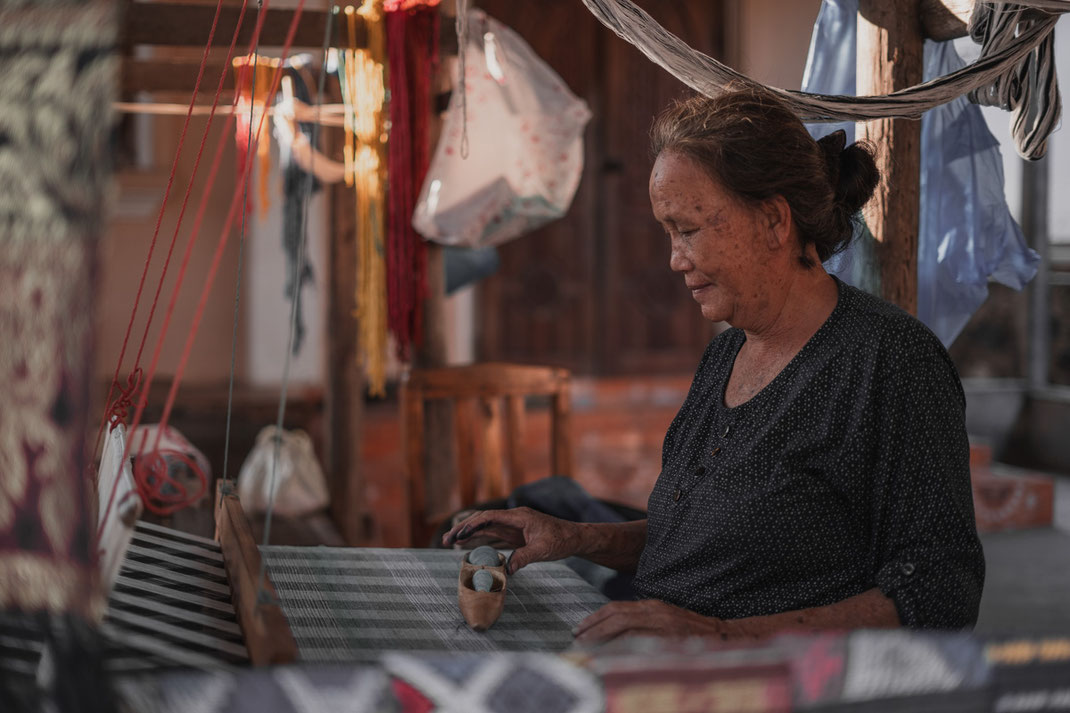 An old woman sits at her loom and works on her fabric.