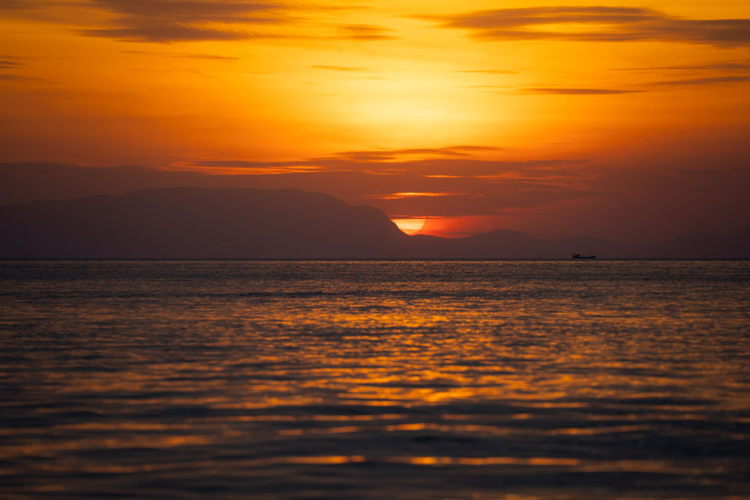 Ein Sonnenuntergang über den Meer mit einer orangen Sonne.