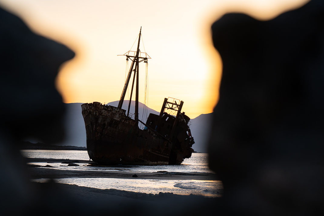 Das alte Schiffswrack zum Sonnenaufgang mit steinernen Mauern im Vordergrund.