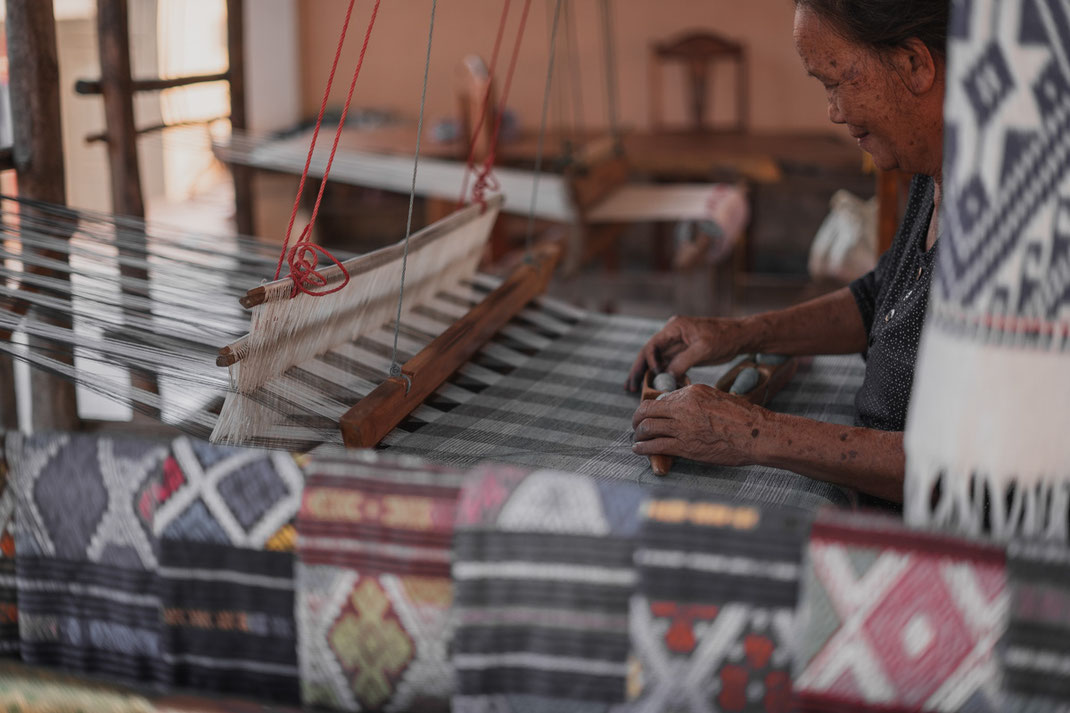 Une vieille femme est assise à son métier à tisser et travaille sur son tissu.