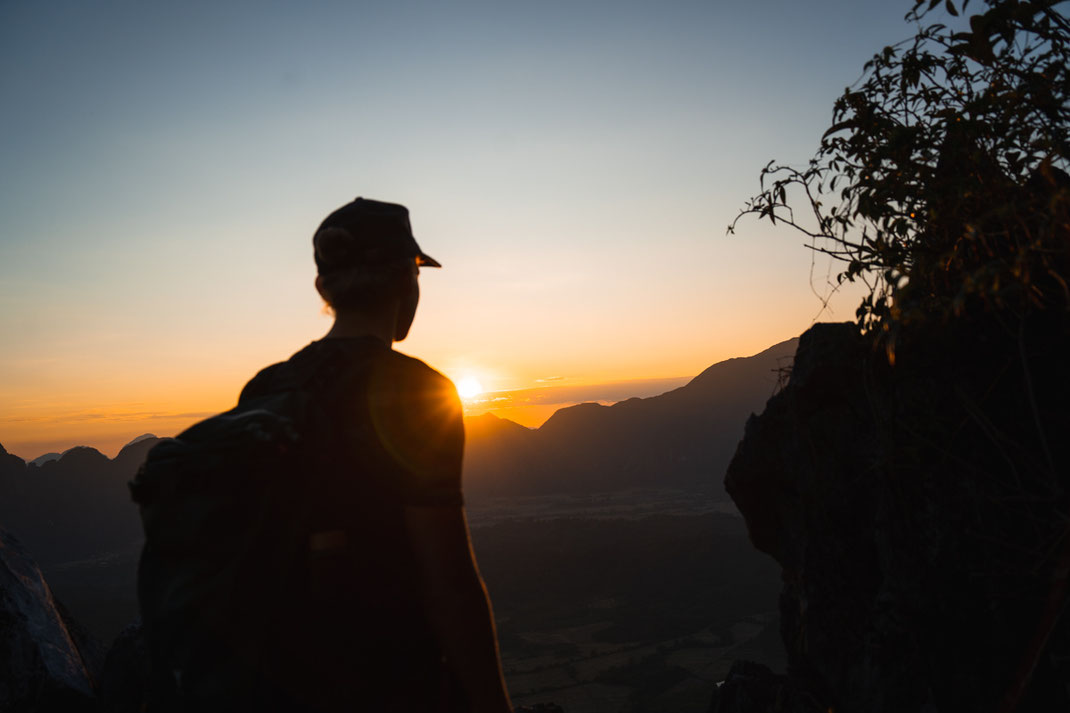 Un homme se tient à un point de vue à Vang Vieng au coucher du soleil.