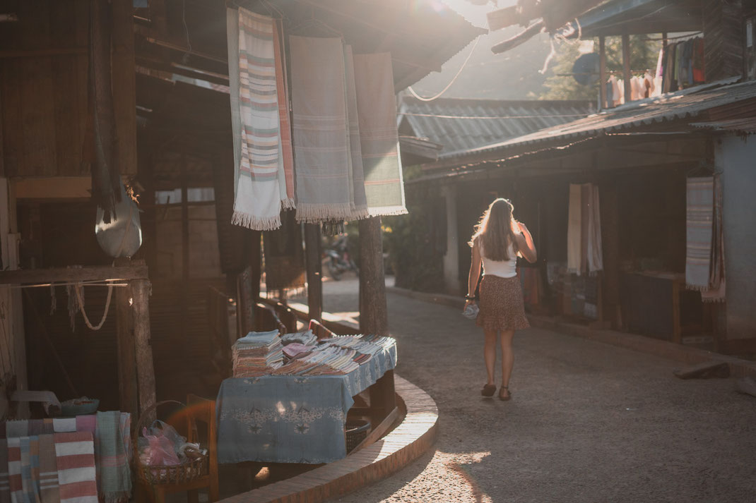 A young woman walks through the weaving village of Ban Xang Hai at sunset.