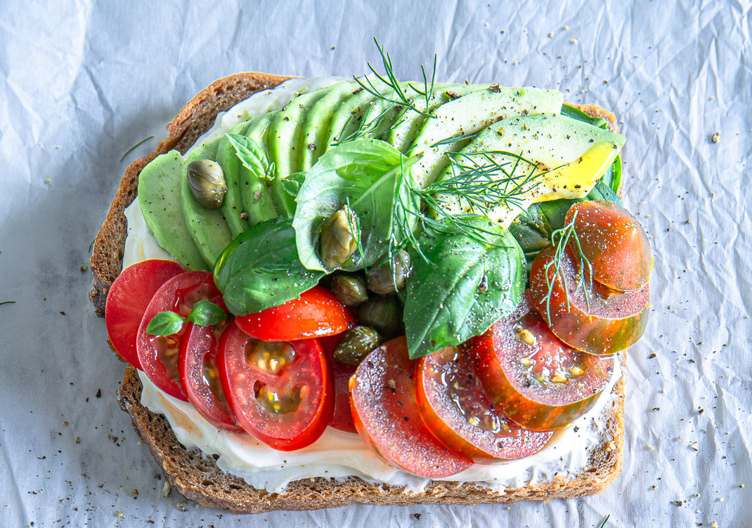 Dinkelvollkornbrot mit cremigem Frischkäse, frischen Tomaten, Avocado und Kräutern