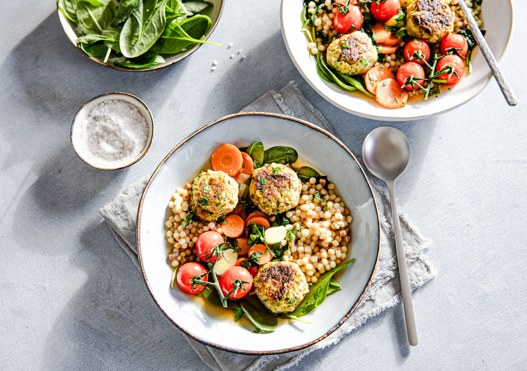 Klare Gemüsesuppe mit knusprigen Gemüsebällchen, Fregola und Babyspinat in einem Suppenteller