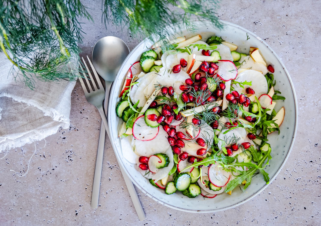 Rettichsalat mit Radieschen, Minigurke und Granatapfelkernen in einer weißen Schüssel angerichtet - mit Dill-Vinaigrette angemacht und frischem Dill als Topping