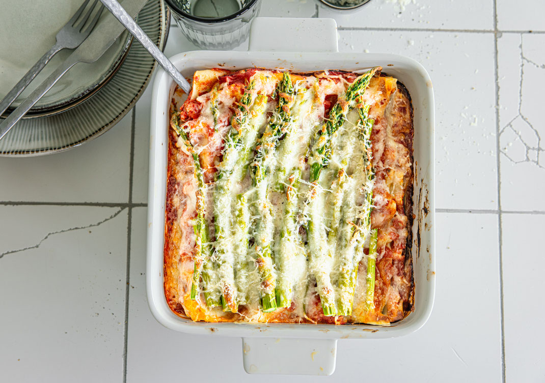 Spargel-Lasagne in einer weißen Auflaufform von oben fotografiert – grüner Spargel deutlich sichtbar unter goldbraunem geschmolzenem Mozzarella