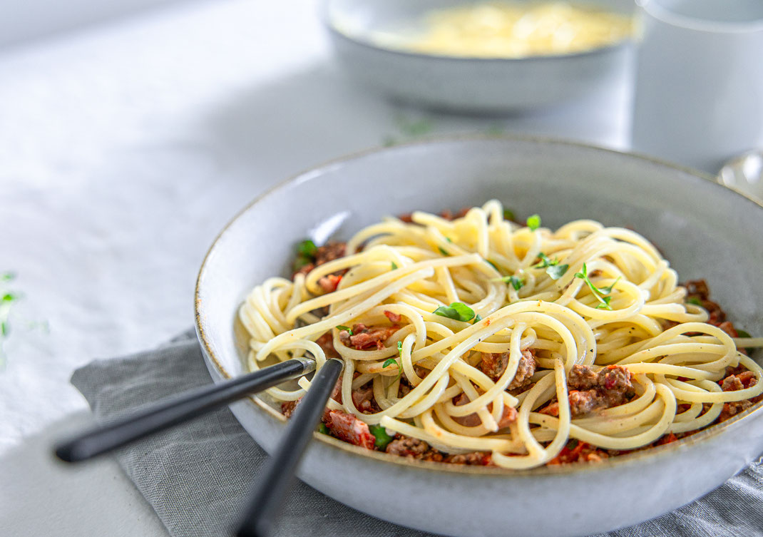 Mediterrane Hackfleisch-Spaghetti mit frischen Kräutern, Erbsen und cremiger Sahnesauce auf einem weißen Teller serviert