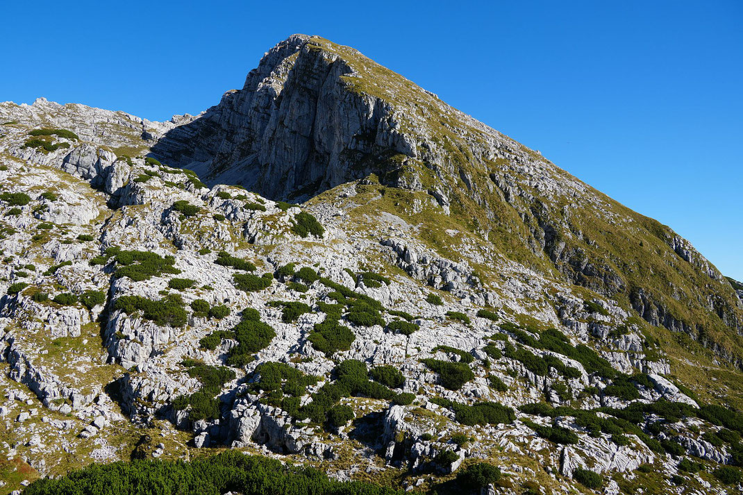 Blick zum Rombon, der Aufstieg führt zunächst im Schatten der Felswände und zieht dann nach rechts hinauf