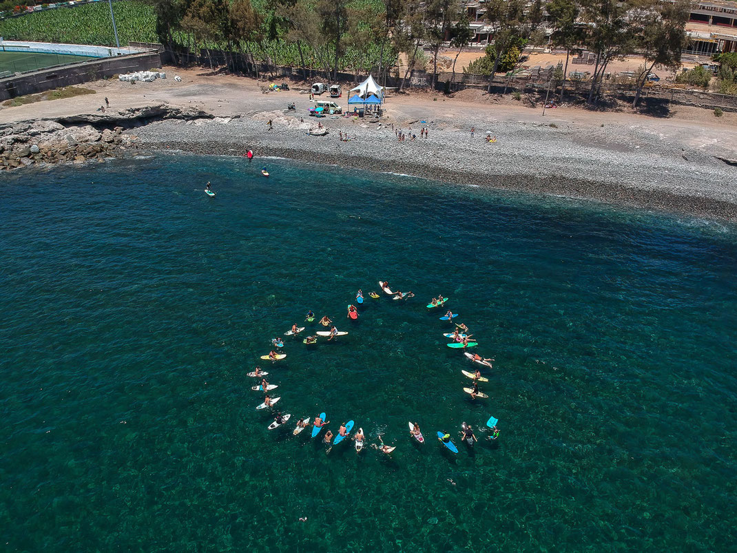 Surfers forming a heart shape on Arguineguín Beach after participating in the annual beach clean, showcasing our commitment to environmental sustainability.