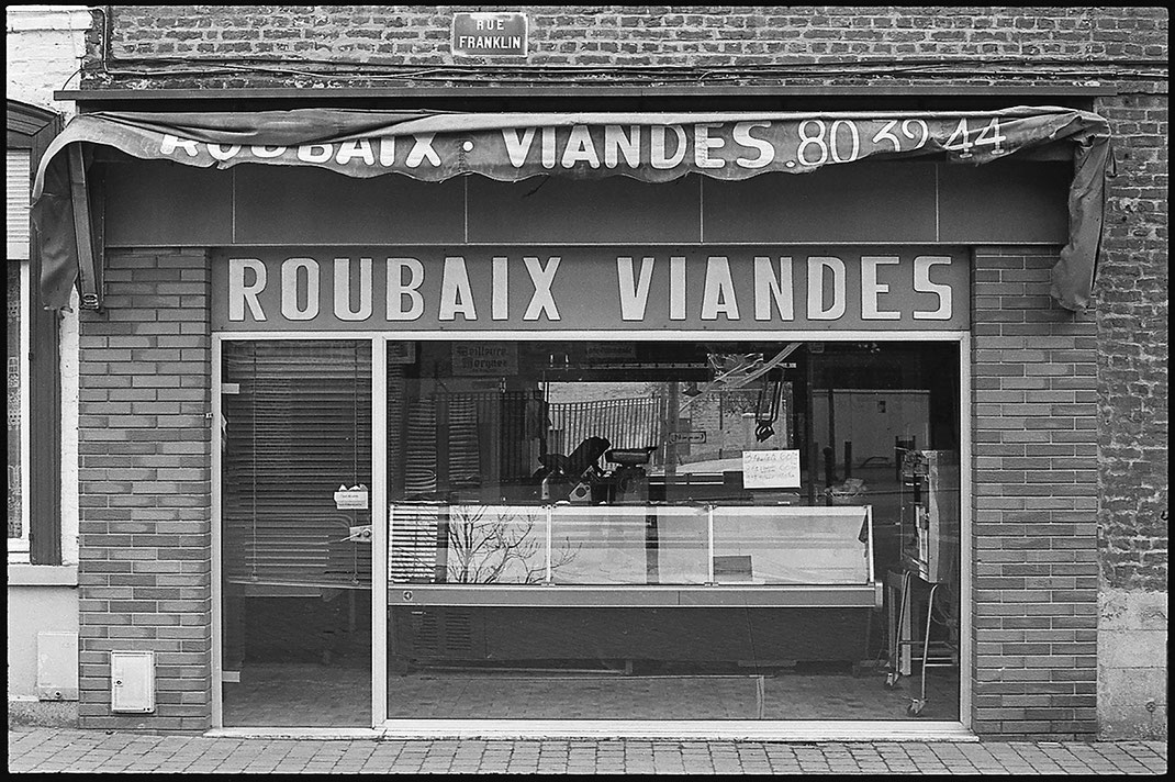 Photographie noir et blanc d'une vitrine de boucherie "Roubaix Viandes" à Roubaix, France.