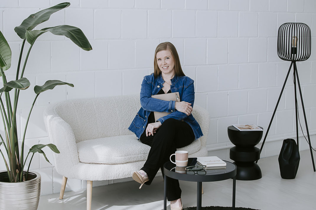 Frua sitzt auf stylischer Sitzgelegenheit mit kleinem Tisch mit Unterlagen in der Hand in einem Loft