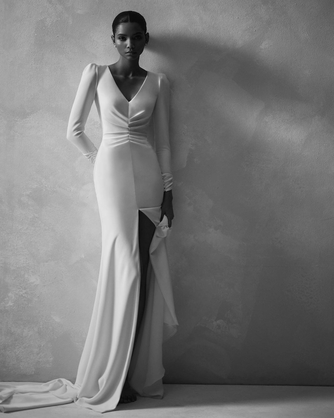 Schöne Frau mit einem Brautkleid von Rosa Clará Couture stehend vor einer Wand