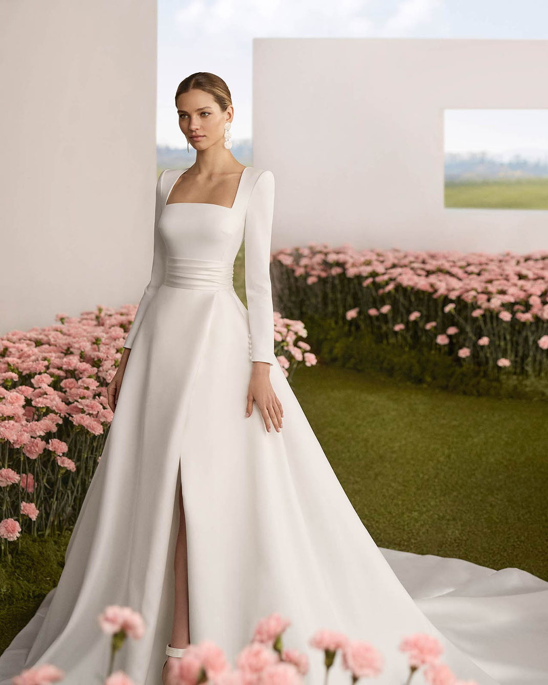 Elegante Frau vor einem rosa Blumenmeer trägt das Brautkleid Rasgo von Rosa Clará Couture