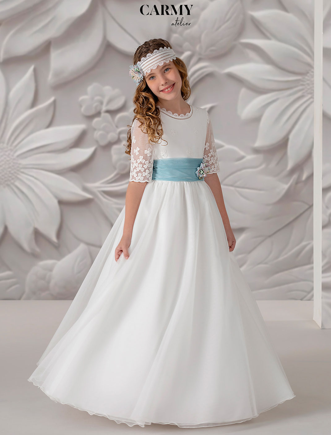 Mädchen mit gelocktem Haar trägt ein Kommunionkleid von Carmy aus der Kommunion Kollektion 2025