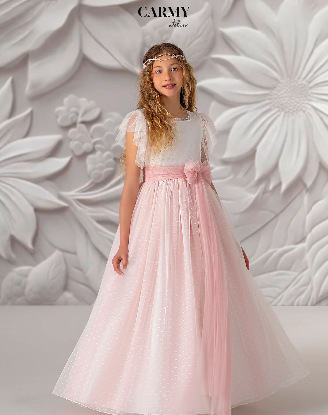 Mädchen mit blonden Locken trägt ein Kommunionkleid aus der Carmy Kommunion 2025 Kollektion