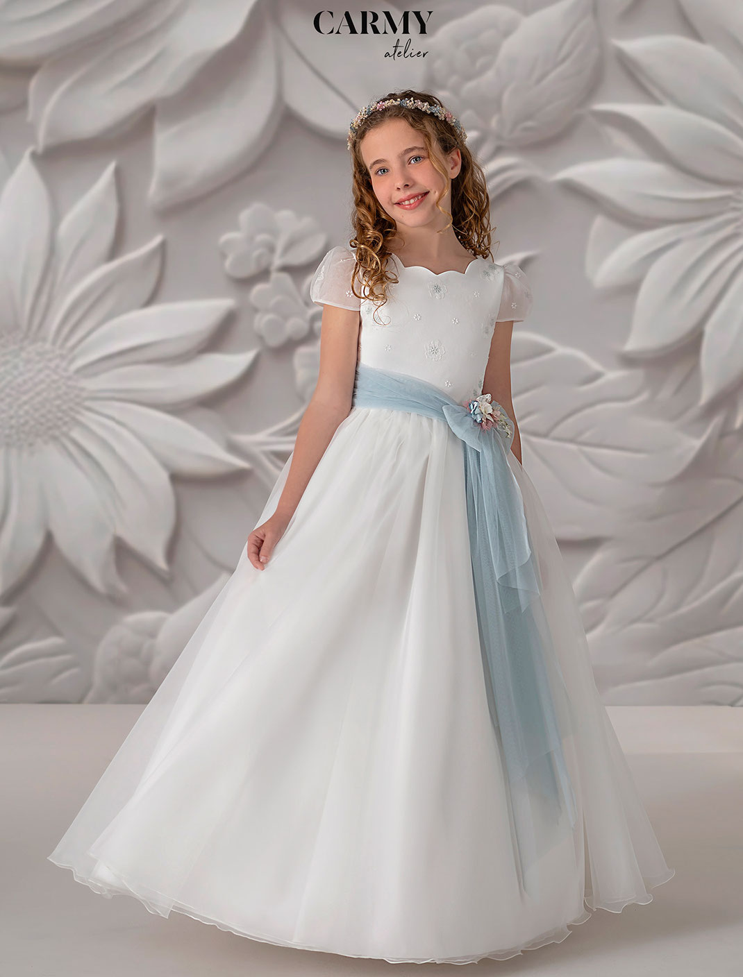 Mädchen trägt ein Kommunionkleid aus zartem Organza Kollektion Carmy Kommunion 2025