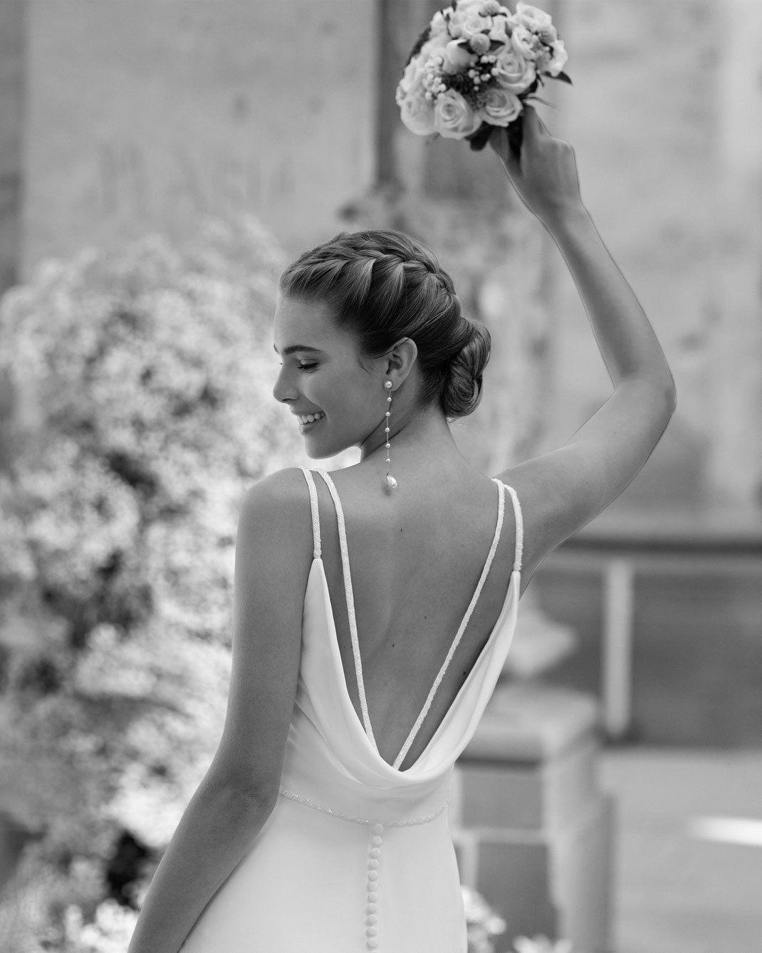 Frau mit Flechtfrisur und Blumenstrauss trägt das Brautkleid Haizea aus der Alma Novia Kollektion 2025