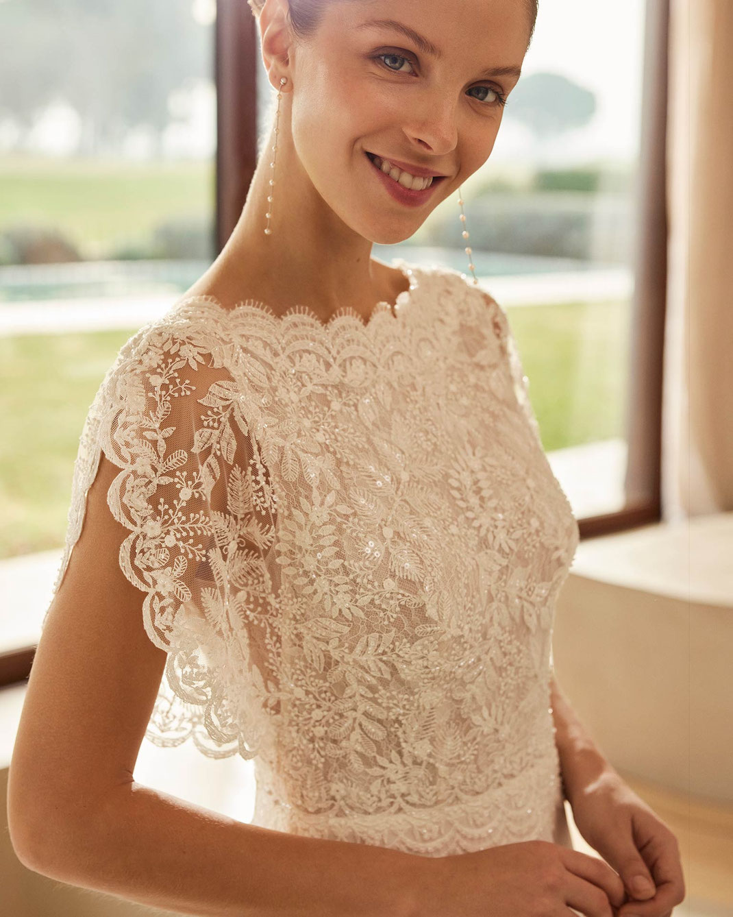 Junge Frau mit Ohrringen von Rosa Clara trägt das Brautkleid Zamina aus der Aire Boho Kollektion 2026