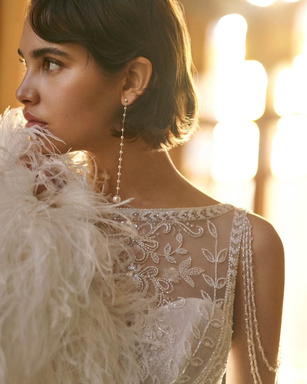 Junge Frau mit weisser Federboa trägt das Brautkleid Bella aus der Rosa Clará Gatsby Kollektion 2026