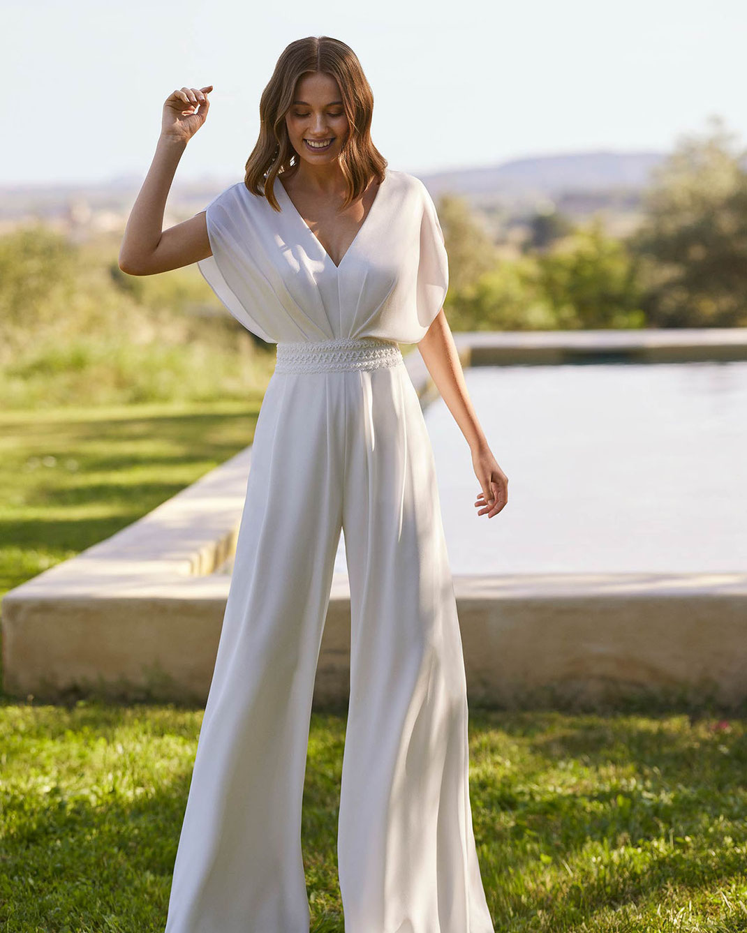 Junge Frau trägt das lange Braut-Jumpsuit Nadira aus der Alma Novia 2026 Kollektion