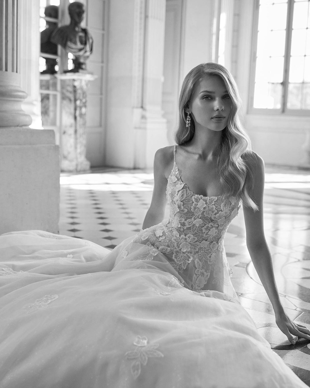 Blondes Top Model sitzend auf dem Parkettboden trägt das Brautkleid Ersel aus der Rosa Clará Dreams Kollektion 2025