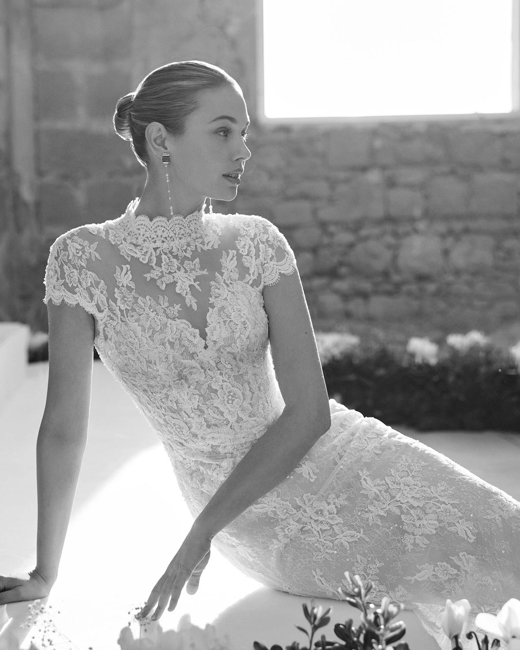 Junge elegante Frau sitzt auf einem Marmorstein und trägt das Brautkleid Marsella aus der Aire Barcelona Kollektion 2026